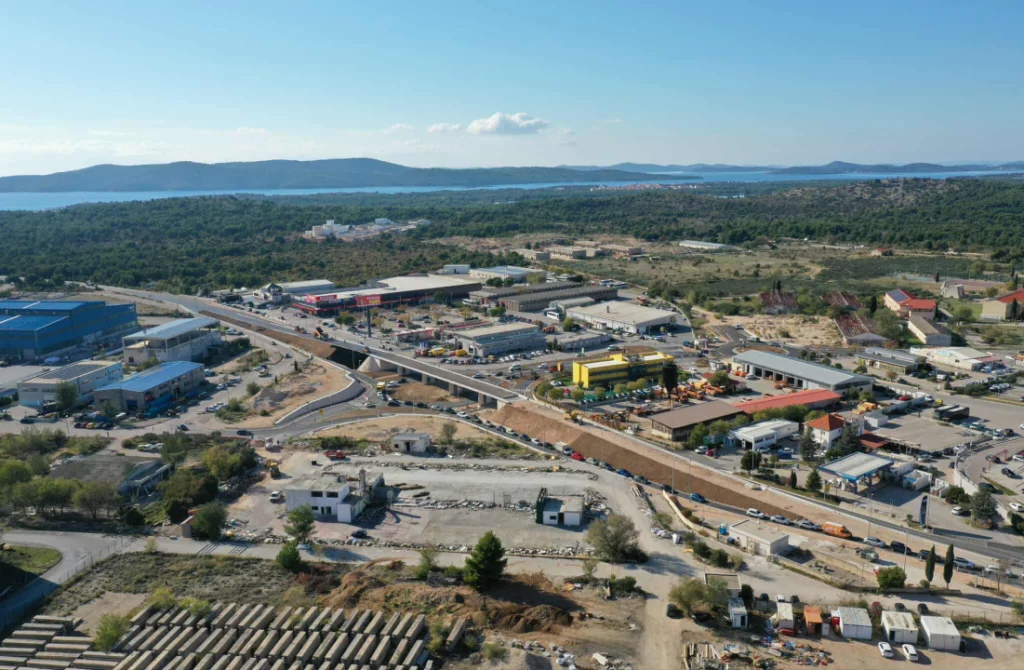 Čelična arterija Dalmacije: Nadvožnjak od 100 metara postaje zvijezda infrastrukturnog preporoda na Jadranu Zračna snimka velikog dalmatinskog gradilišta s pogledom na dovršeni nadvožnjak od 100 metara, simbol infrastrukture Dalmacije.
