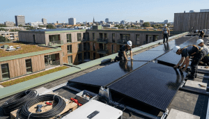 Građevinski radnici u zaštitnoj opremi instaliraju solarne panele na ravni krov moderne stambene zgrade, simbolizirajući standarde zelene gradnje u 2026.