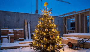 Osvijetljeni božićni bor s toplim lampicama stoji unutar nedovršene konstrukcije na snijegom prekrivenom gradilištu u sumrak